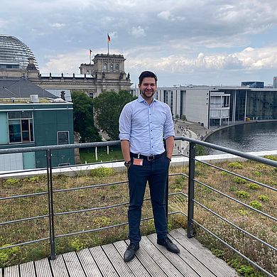 Jannis Bronisefski steht auf der Terrasse eines Abgeordnetenbüros mit Blick auf das Reichstagsgebäude